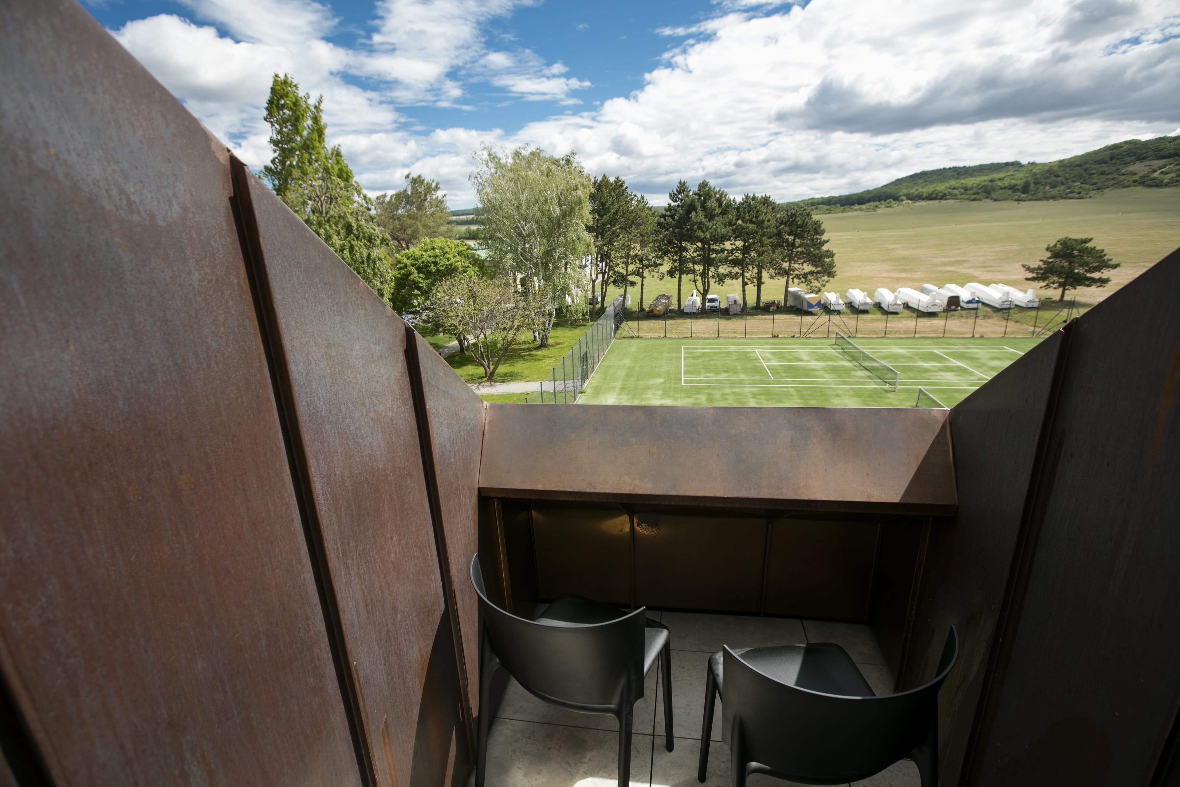 View from a balcony at Hotel Spitzerberg by b_smart of a tennis court and a tree-surrounded landscape under a cloudy sky